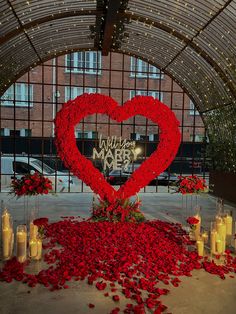 a red heart surrounded by candles and flowers in front of a building with large windows