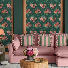 a pink couch sitting in front of a green wall with flowers on it and a wooden coffee table