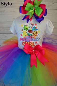 the birthday girl is wearing a white shirt and colorful tutule with a large bow