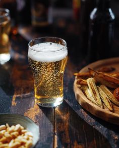 a wooden table topped with plates of food and glasses filled with beer next to pretzels