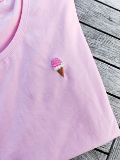 an ice cream cone embroidered on the back of a pink t - shirt that is sitting on a wooden table