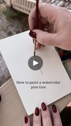 a person holding a pen and writing on a piece of paper with the words how to paint a watercolor pine tree