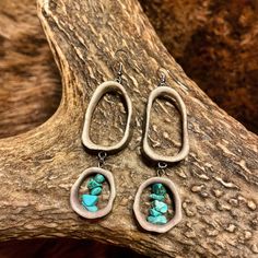 two earrings with turquoise stones are hanging from a tree branch