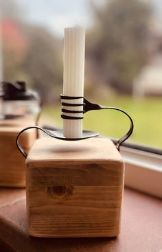 a wooden block with a white candle in it sitting on a window sill next to a pair of glasses