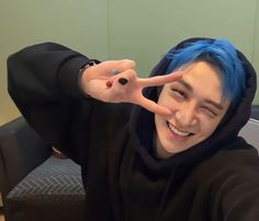 a person with blue hair making the peace sign