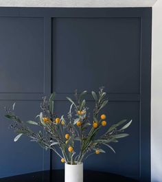 a white vase filled with yellow flowers on top of a black table next to a blue wall