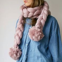 a woman wearing a pink scarf with pom - poms on her neck and blue shirt