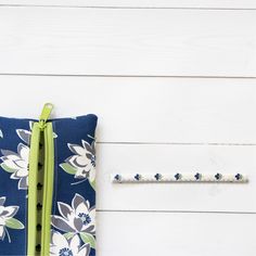 a blue and white flowered pillow next to a green zippered pencil case on a white wooden surface