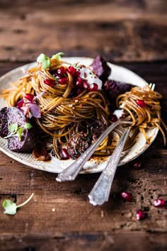 a white plate topped with spaghetti and meat covered in pomegranate next to silverware