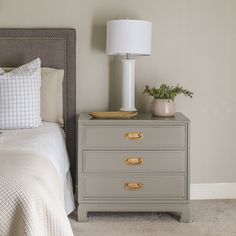 a nightstand with two drawers and a lamp next to it on top of a bed