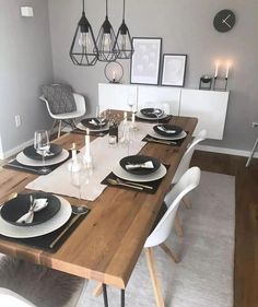 the dining table is set with black and white plates, place settings and candles on it