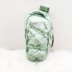 the north face green backpack is laying on top of a fluffy white rug and it's zippered up