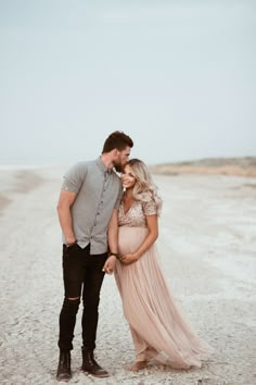 a man and woman standing next to each other on a dirt road in front of the ocean