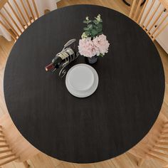 a black table topped with a white plate and wine bottle next to a vase filled with flowers