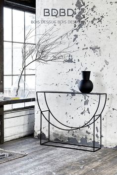 a black vase sitting on top of a metal table next to a wall with peeling paint