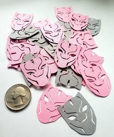 a pile of pink and grey paper masks next to a penny on a white surface