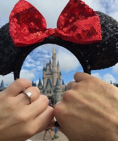 two hands holding mickey mouse ears in front of a castle with red sequins