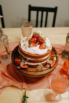 there is a cake with strawberries on it sitting on the table next to glasses