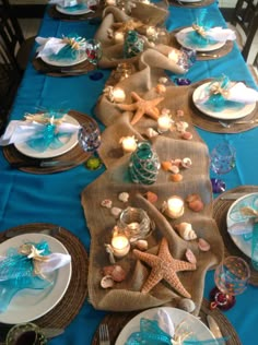 the table is set with blue and white plates, silverware and starfish decorations