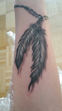 a black and white photo of a feather on someone's arm with chains attached to it