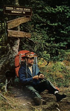 a man sitting on the ground in front of a wooden sign pointing to different destinations