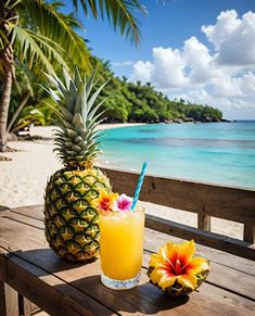 two pineapples and an orange drink sit on a wooden table near the ocean