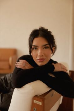 a woman sitting in a chair with her arms folded over her chest and looking at the camera