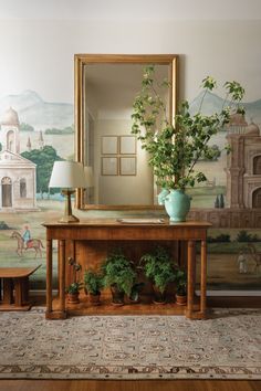 there is a mirror and some potted plants in front of a table with a lamp on it