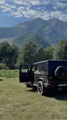 a black jeep parked on top of a lush green field next to a mountain range