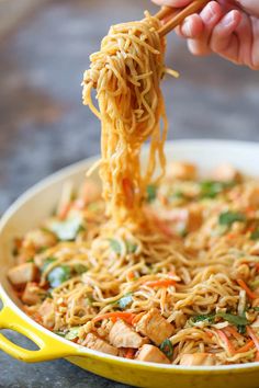 someone is eating noodles with chopsticks in a yellow pan on a table top