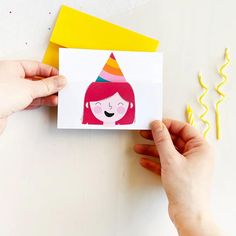 someone holding up a card with a drawing of a girl wearing a party hat on it