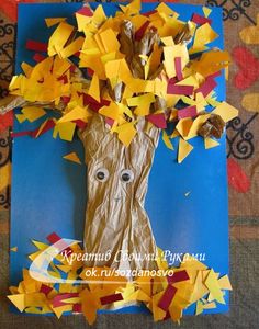 a tree made out of tissue paper on top of a blue board with yellow and red leaves