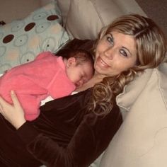 a woman holding a baby in her arms and smiling at the camera while sitting on a couch