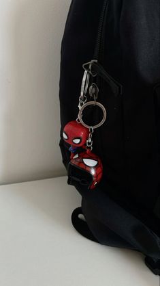 a spiderman keychain hanging from the side of a black backpack with a red and white face on it