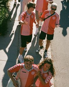 a group of people in red and white uniforms running down the street with tennis rackets