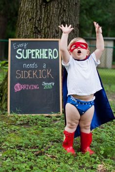 a baby dressed as superman standing in front of a sign