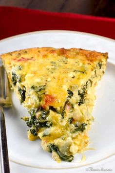 a slice of quiche with spinach and cheese on a plate next to a fork