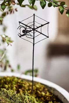 a wire sculpture is placed on top of moss in a pot with a plant growing out of it