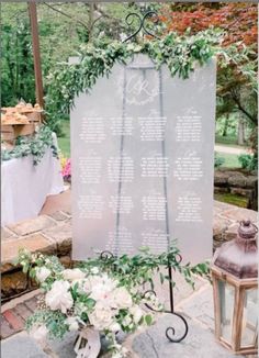 a wedding ceremony sign with flowers and greenery on the side of it next to a lantern