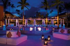 an outdoor seating area with candles lit up in the background and palm trees around it