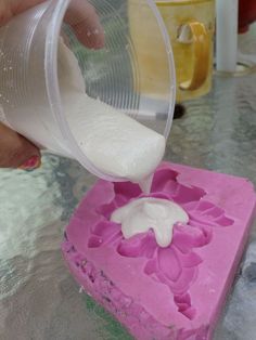 someone pouring white liquid into a pink square shaped object with flowers on it's side