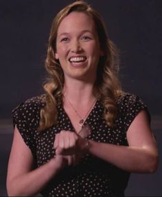 a woman is smiling and holding her hands together