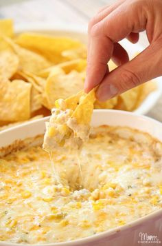 a hand dipping a tortilla chip into a bowl of cheesy dip