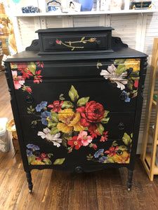 an old dresser painted with flowers and leaves on the front, sitting in a store