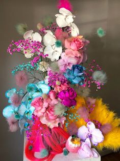 a vase filled with flowers and feathers on top of a wooden table next to a wall