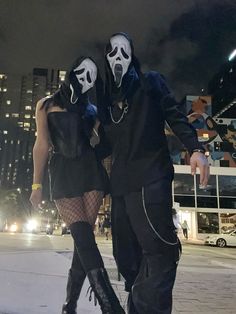 two people dressed in black and white are walking down the street with their faces covered by masks