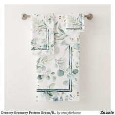 two towels hanging on a towel rack in front of a white wall with green leaves