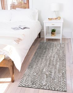 a white bed sitting in a bedroom next to a wooden table with a potted plant on top of it