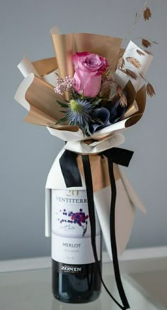 a wine bottle wrapped in brown paper with a pink rose