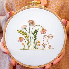 a person holding up a small embroidery hoop with an animal and flowers on it's side